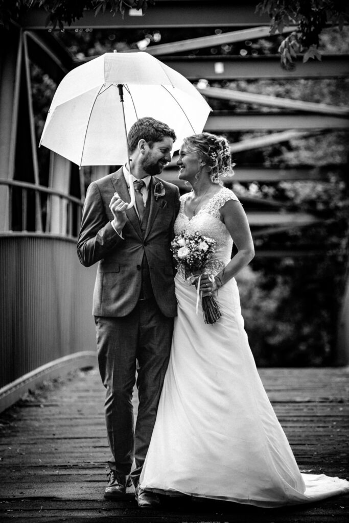 Bride and groom crossing bridge in rain