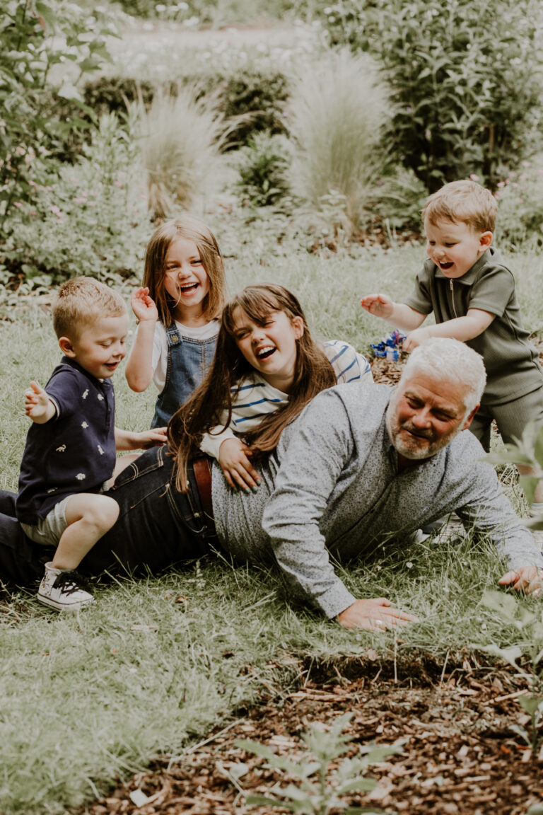 grandad with grandkids on family shoot, laughing and climbing on him