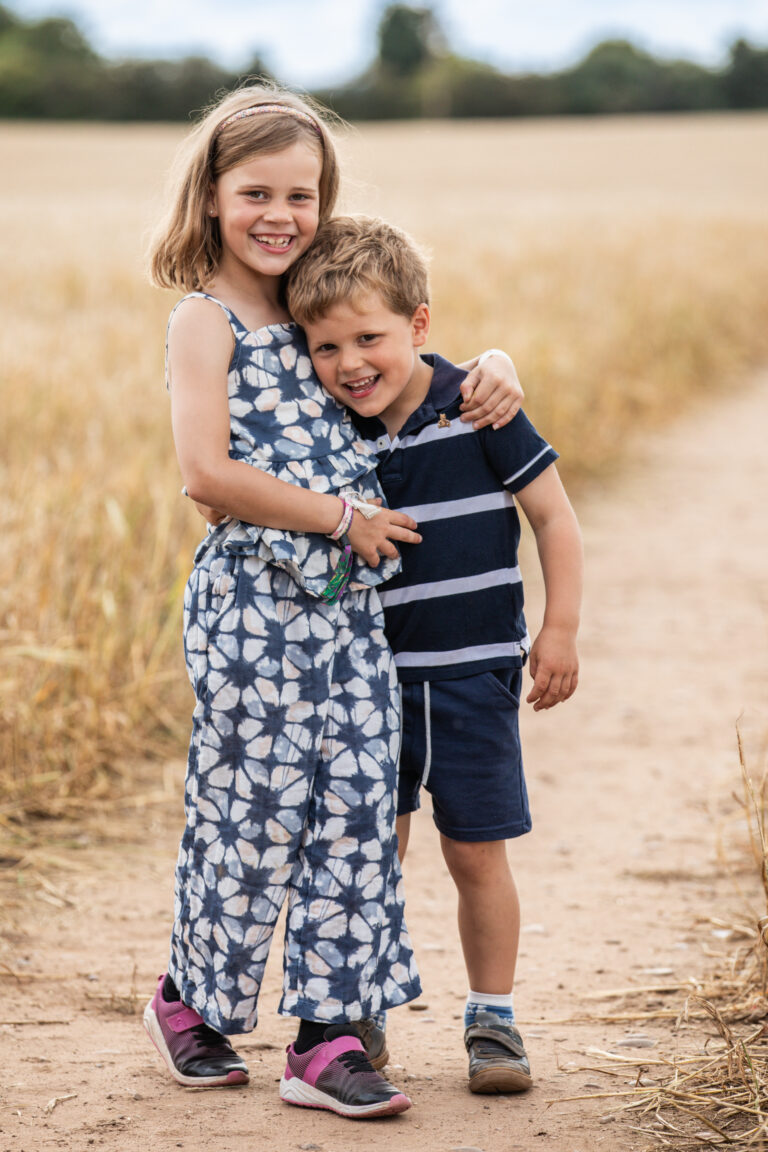 brother and sister in golden corn field smiling