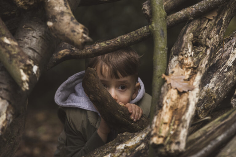 boy peaking through trees in family shoot